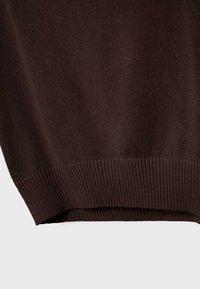 Gros plan sur l'ourlet d'un pull en maille marron foncé avec un motif côtelé sur un fond clair.