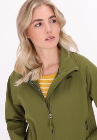 Olivinės spalvos softshell striukė su aukštu apykakle ir užtrauktuku. Išskirtiniai bruožai - skėčio logotipas ant krūtinės ir dryžuota geltona marškinėliai po sijonu.