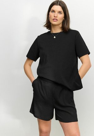 Black cotton T-shirt with short sleeves, paired with black, textured shorts. Relaxed fit, featuring side pockets and an elastic waistband.