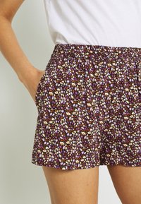 Floral shorts featuring a dark purple background with small white, orange, and lavender flowers. Elastic waistband with side pockets.