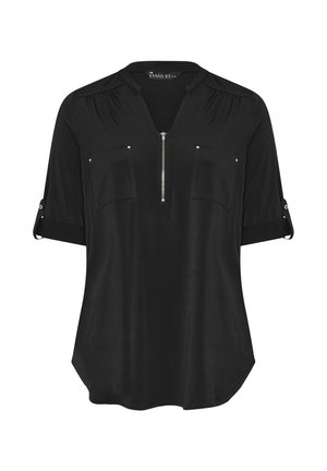 Blusa negra con cierre frontal, dos bolsillos en el pecho y mangas enrolladas. Confeccionada en una tela suave y con un dobladillo ligeramente curvado.