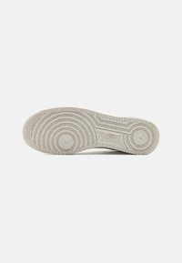 White sneaker bottom featuring a textured rubber sole with circular patterns and a small Nike logo embossed near the heel area.