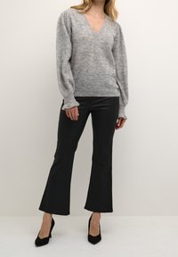 Szary sweter z dekoltem w kształcie litery V o fakturowanym splocie i bufiastych rękawach, w połączeniu z czarnymi spodniami w kształcie dzwonów i czarnymi szpilkami. Minimalistyczny design.