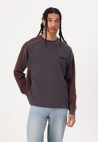 Langærmet sweatshirt med en struktureret, ribbet design i mørkegrå og brun, med kontrasterende ærmer og et lille logo på brystet.