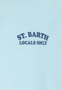 Camiseta azul claro con texto azul oscuro que dice "SÓLO LOCALES DE ST. BARTH" en una fuente negrita y curvada. Material de algodón suave.