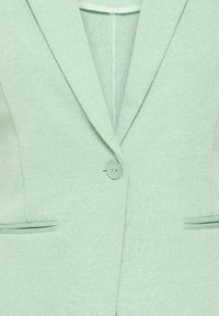 Blazer vert pastel à un seul bouton avec revers crantés et poches frontales horizontales en tissu texturé.