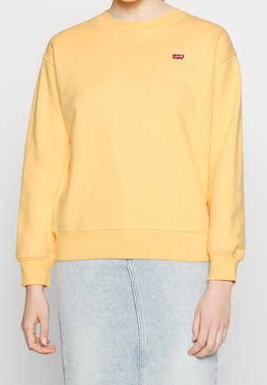 Felpa gialla di cotone con maniche lunghe, polsini a coste e una piccola etichetta con il logo Levi's sul petto. Abbinata a una gonna di jeans azzurri.
