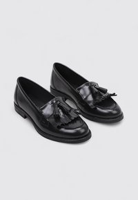 Mocasines de cuero negro con un acabado suave, que cuentan con un acento decorativo de flecos en la parte frontal y un tacón bajo para mayor comodidad.