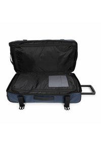 Bolsa de viaje azul de material blando con interior negro, doble cremallera y asa retráctil. Cuenta con un bolsillo de almacenamiento gris en el interior.