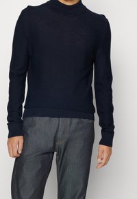 Marinblå crewneck-tröja med ribbad kant, tillverkad av mjukt stickat material. Har en subtil logotyp på bröstet och figursydda ärmar.