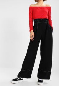 Rode off-the-shoulder lange mouwen top gecombineerd met hoge taille zwarte wijde broek met een ceintuur en witte stiksels. Zwarte sneakers.