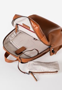 Zaino in pelle marrone con finitura testurizzata, dotato di un interno con motivo geometrico e una piccola pochette abbinata. Chiusure a zip visibili.