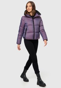 Puffer jacket in iridescent purple and black, featuring a zip front, hood, elastic cuffs, and side pockets. Worn with black pants and boots.