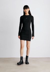 Black long-sleeve bodycon dress with a round neckline, made of smooth fabric, paired with black ankle boots featuring chunky soles.