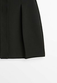 Jupe noire jusqu'au genou avec plis devant et détails de coutures visibles.