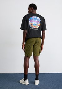 Black graphic t-shirt featuring colorful candy print on the back, paired with olive-green cargo shorts and white sneakers.