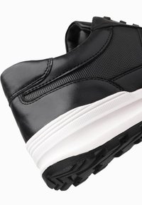 Sneaker nera con tomaia in pelle liscia, dettagli in rete testurizzata e una spessa suola intermedia bianca. La suola in gomma presenta un battistrada con motivo.