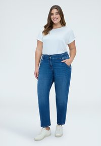 Jean en denim bleu à taille haute, coupe décontractée, cinq poches et léger effet délavé, assorti à un haut blanc uni à manches courtes et des baskets blanches.