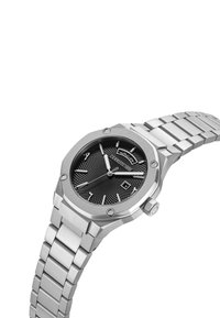 Reloj de acero inoxidable con caja octagonal y esfera negra texturizada. Presenta manecillas plateadas, índices horarios y una pantalla de fecha. Pulsera de metal.