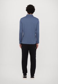 Langærmet, lyseblå polo-shirt parret med sorte cargobukser. Outfittet har en afslappet pasform og funktionelle lommer på bukserne.
