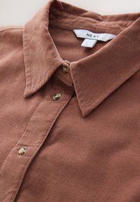 Barna kordbársony ing gombos elülső résszel, hegyes gallérral, és kontrasztos világos gombokkal, bordázott texturált anyagból.