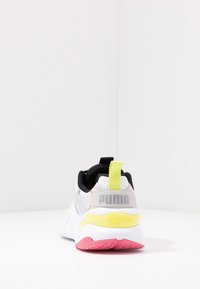 Białe sneakersy z czarnymi akcentami, z siateczkowego materiału, żółta pętla na pięcie, różowa podeszwa i srebrne logo. Wyraźne detale systemu R na pięcie.