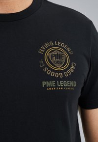 Zwarte katoenen t-shirt met een ronde halslijn, korte mouwen en een grafische print aan de voorkant met "PME LEGEND" en "FLYING LEGEND" in goud en groen.