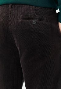 Close-up of dark brown corduroy pants with a buttoned back pocket worn with a green sweater.