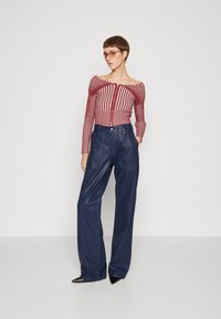 Red and white striped cropped sweater with a zip front, paired with navy leather wide-leg pants. Model wears sunglasses and has short hair.