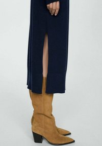 Vestido azul marino con una abertura lateral, combinado con botas altas hasta la rodilla de ante color camel, con puntera puntiaguda y tacón grueso.