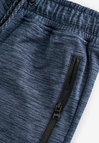 Námorné športové joggers nohavice s textúrovanou tkaninou, ktoré majú elastický pás, nastaviteľnú šnúrku a bočné vrecko na zips.