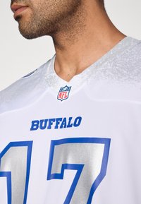 Balta formas kreklu ar zilām burtiem "BUFFALO" un sudraba numuru "17." NFL logotips uz apkakles, teksturēts audums un apaļa kakla izgriezuma dizains.