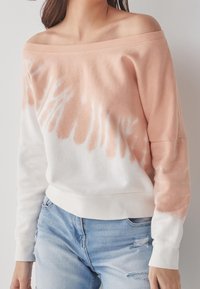 Mikina bez ramene ve světle broskvové a bílé barvě, s motivem tie-dye, dlouhými rukávy a měkkou, texturovanou tkaninou.