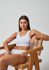 Grijze katoenen sportbh met een brede elastische band met het label "SNOCKS," gecombineerd met bijpassende slipjes, tegen een lichte achtergrond op een houten stoel.