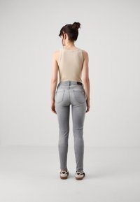 Top sin mangas beige claro combinado con jeans gris ajustados, con bolsillos traseros y cintura alta; llevado con zapatillas negras y blancas.