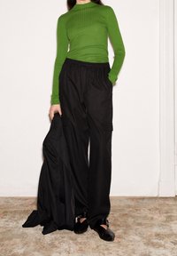 Vihreä ribbineulottu pitkähiha-yläosa yhdistetty mustiin taskullisiin cargo-housuihin, pidetään mustalla takilla ja mustilla mules-kengillä, joissa on solkikoriste.