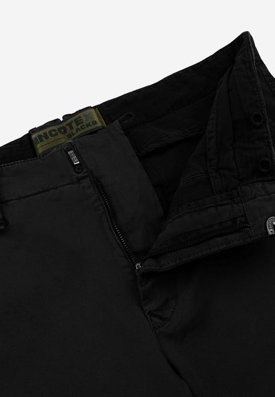 Pantaloni neri con una texture liscia, dotati di una chiusura lampo, chiusura a bottone nascosta e un'etichetta verde all'interno della vita.