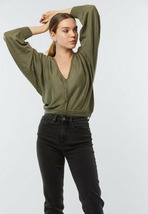 Haut vert olive à boutons avec un décolleté en V profond, des manches larges et un ourlet ajusté, assorti à un jean noir taille haute. Texture lisse.