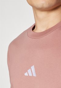 Roze katoenen t-shirt met een ronde hals en korte mouwen. Het heeft een wit geborduurd Adidas-logo op de linkerborst.