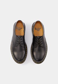 Pantofi din piele neagră cu vârf rotunjit, design cu șireturi, cusături galbene și o branț moale cu branding vizibil pe căptușeală.