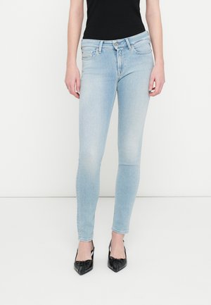 Φωτεινό μπλε στενά τζιν κατασκευασμένα από ντένιμ, με κλασικό σχέδιο πέντε τσεπών και φερμουάρ με κουμπί στο μπροστινό μέρος. Φορεμένα με μαύρα ψηλοτάκουνα παπούτσια.