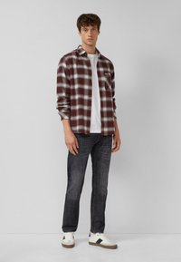 Kariertes Flanellhemd in Dunkelrot und Weiß, getragen über einem weißen T-Shirt, kombiniert mit dunklen Jeans und weißen Sneakern mit schwarzen Akzenten.