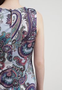 Ärmellös klänning i ljusblått tyg med intrikata paisleymönster i lila, grönt och rosa. Inkluderar en detalj med slits bak.