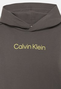 Sweatshirt cinza com capuz, apresentando um destaque do logótipo amarelo "Calvin Klein" no peito, feito de um tecido macio e texturizado.