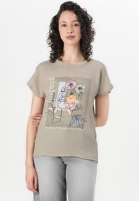 T-shirt beige à manches courtes présentant un design graphique floral aux couleurs pastel et avec du texte. Texture lisse, coupe décontractée, encolure ronde.