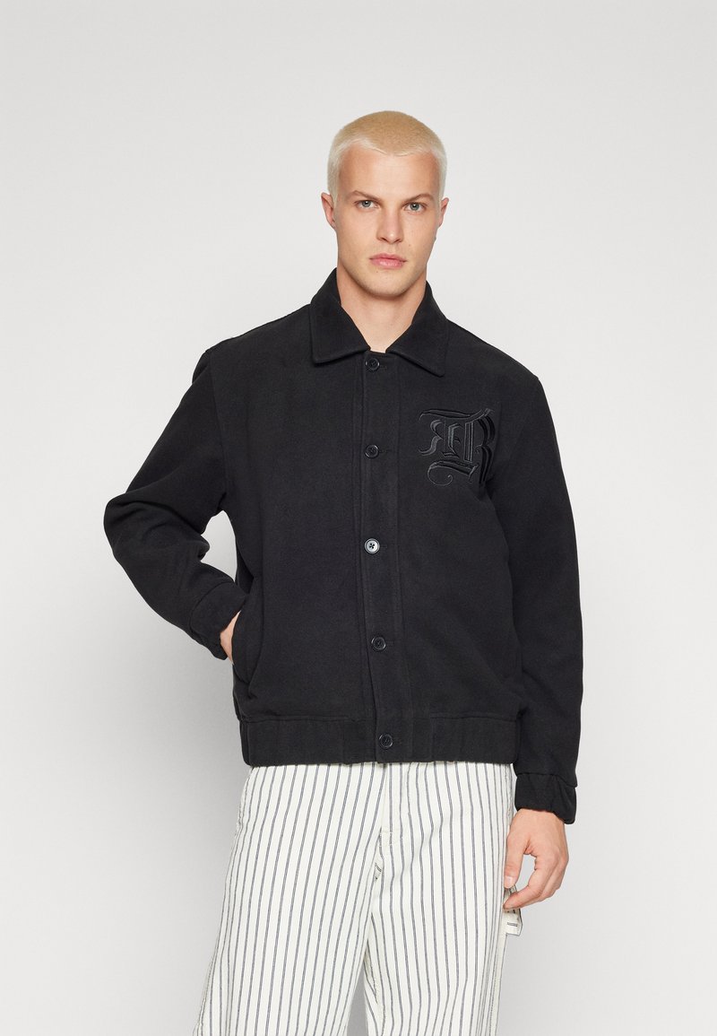 Sort uldjakke med knapper fortil, spidse kraver og sidelommer. Har et tekstureret broderet logo på brystet.