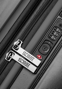 Maleta rígida negra con cremallera y etiquetas de marca en plata, que cuenta con un candado de combinación aprobado por la TSA y una superficie texturizada para mayor durabilidad.
