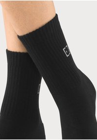 Black ribbed ankle socks with a contrasting logo detail, featuring a smooth texture and a snug fit around the ankle.