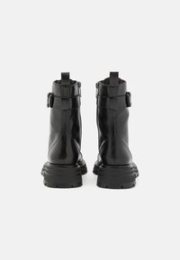 Botas de tobillo de cuero negro con suela de goma gruesa, cierre de cremallera y detalle decorativo de hebilla en el lateral. Textura suave y diseño elegante.