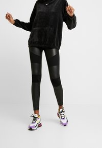 Svart kordfläks hoodie med framficka och ribbade muddar, parat med svarta leggings som har färgblockerade paneler. Mångfärgade sportskor.